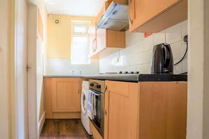 A compact kitchen with wooden cabinets, a built-in oven, a microwave, and a kettle. - Travellers Economic Stays in Orrell Park (Liverpool)
