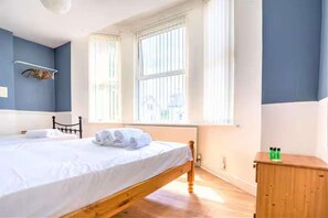 A bedroom with a wooden bed, a wooden nightstand, and a window with blinds. - Travellers Economic Stays in Orrell Park (Liverpool)