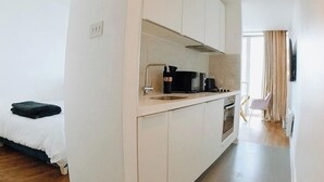 Een kleine keuken met een spoelbak, fornuis en magnetron. Een bed is links zichtbaar.