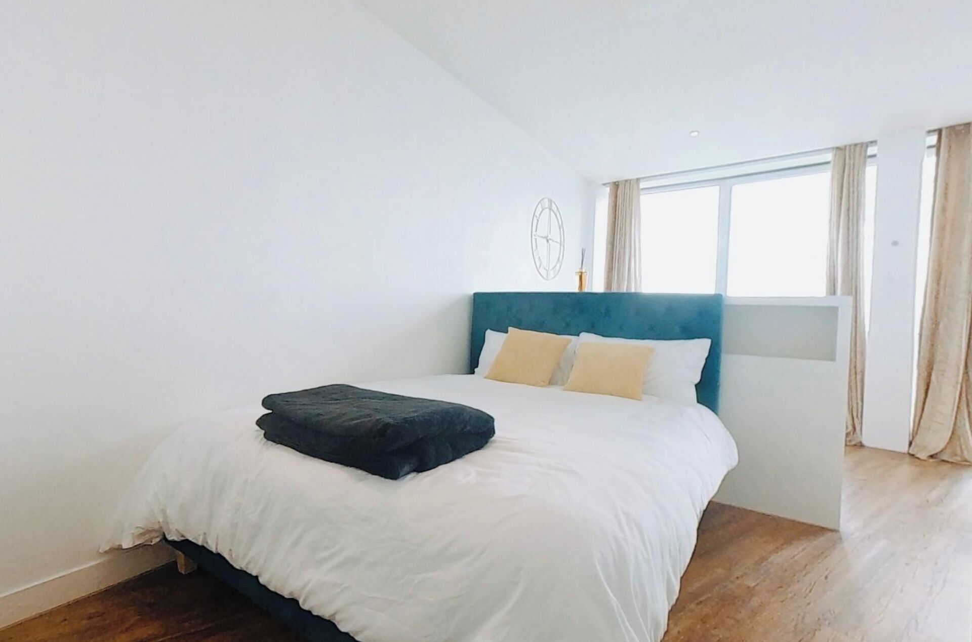 A bedroom with a bed, white bedding, a blue headboard, and a window with curtains.