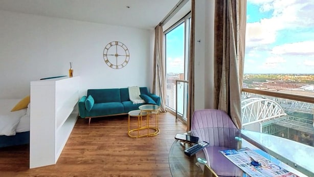 Een moderne woonkamer met een blauwgroene bank, een glazen salontafel en uitzicht op een brug.