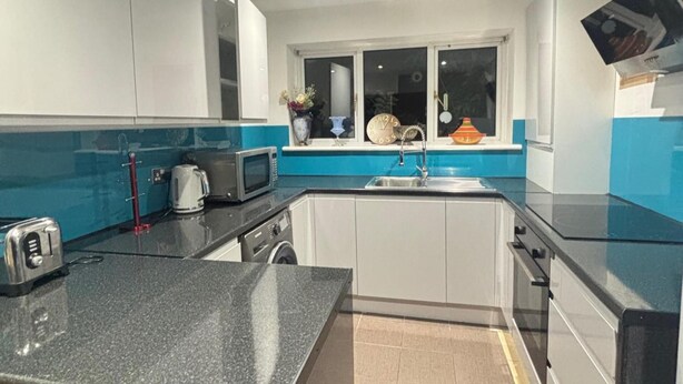 A compact kitchen with a granite countertop, white cabinets, a microwave, a kettle, and a sink. - Woodland Retreat in High Wycombe (High Wycombe)