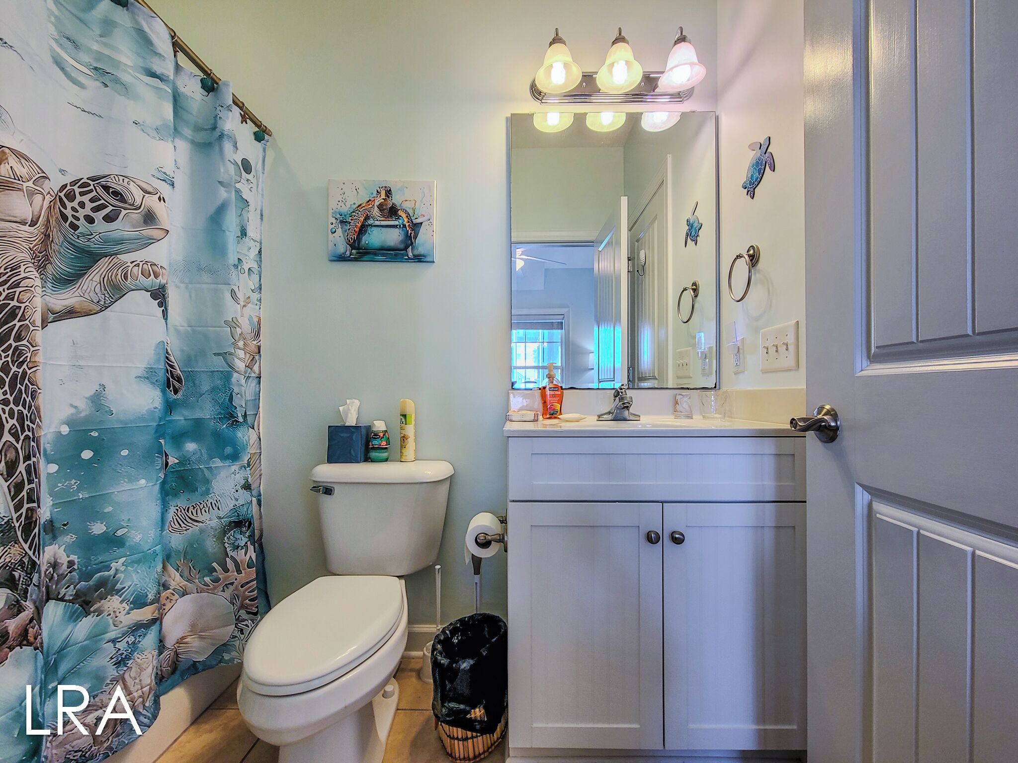 A bathroom with a toilet, sink, and shower curtain featuring sea turtle designs.