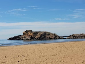 Una playa arenosa con formaciones rocosas y un puente.