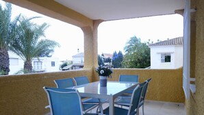 A covered patio with a table and chairs, a flower vase, and a view of surrounding buildings and trees. - Apartments Taravilla 3D P26, in Bahia Beach (Puerto de Mazarrón)