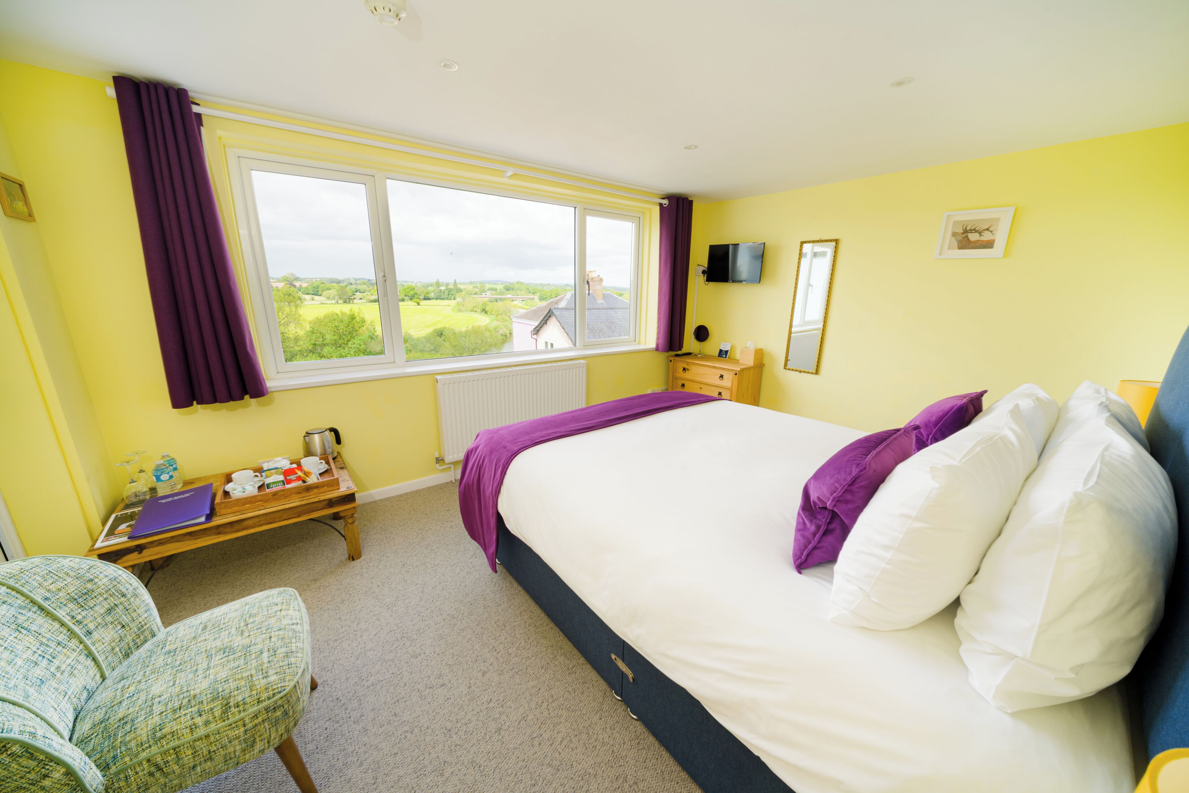 A bedroom with a large bed, a window with a view, a bedside table, and a chair.
