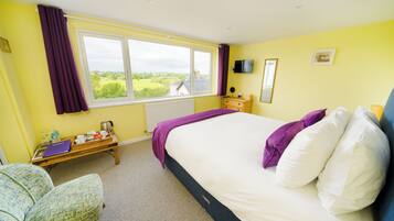 A bedroom with a large bed, a window with a view, a bedside table, and a chair.