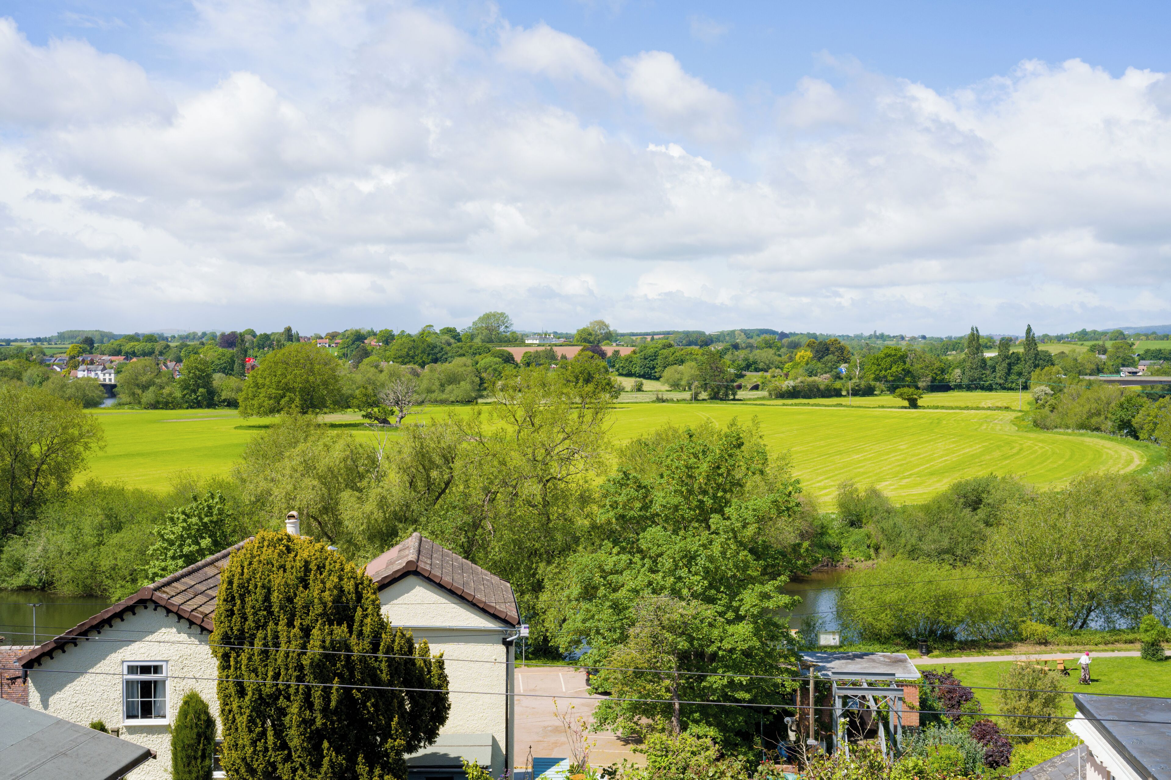 A rural landscape with a house, a river, and a green field.