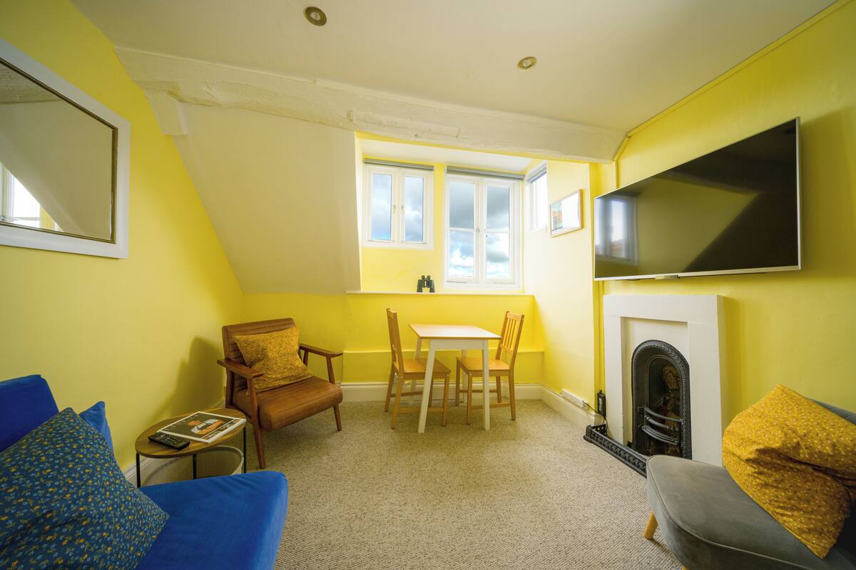 A room with a fireplace, a television mounted on the wall, a dining table with chairs, and a sofa.