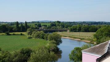 Un río con un puente, campos verdes y árboles.