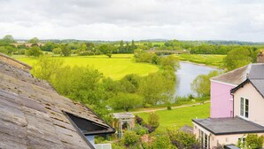A view of a river, green fields, and a pink building with a roof.