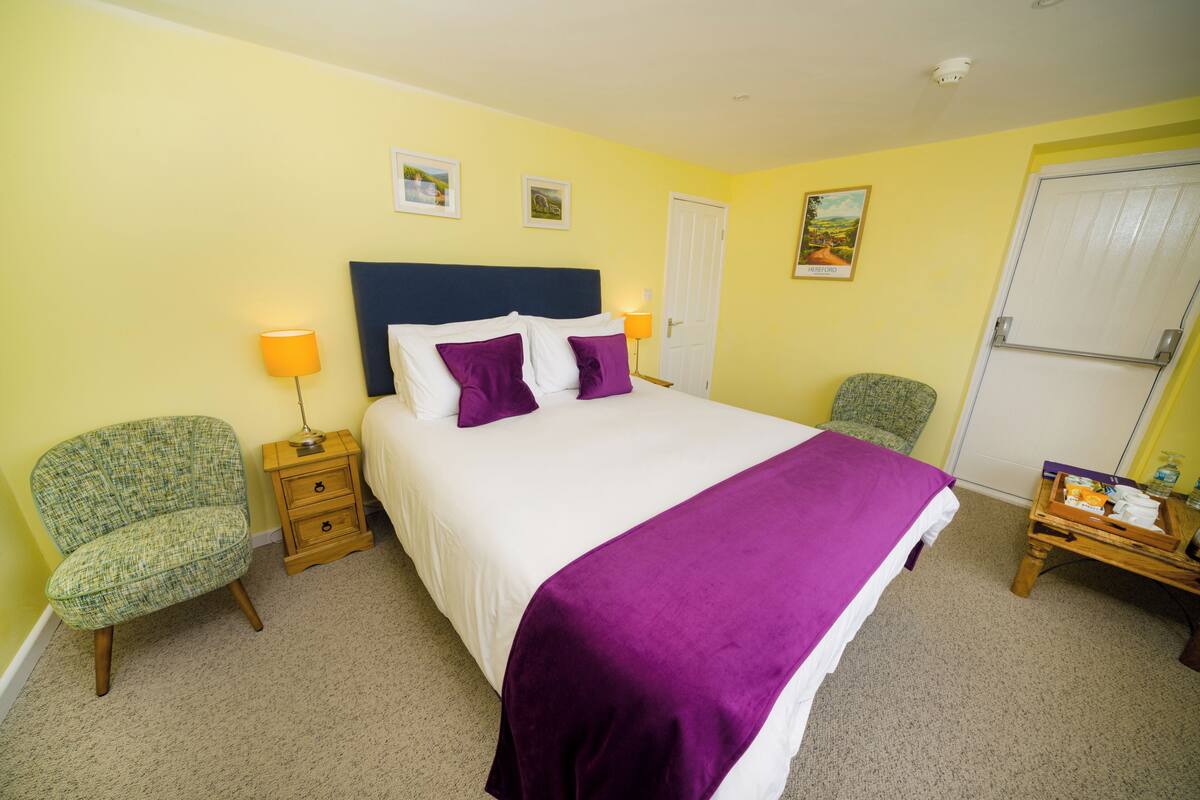 A bedroom with a bed, two bedside tables, a chair, and a door.