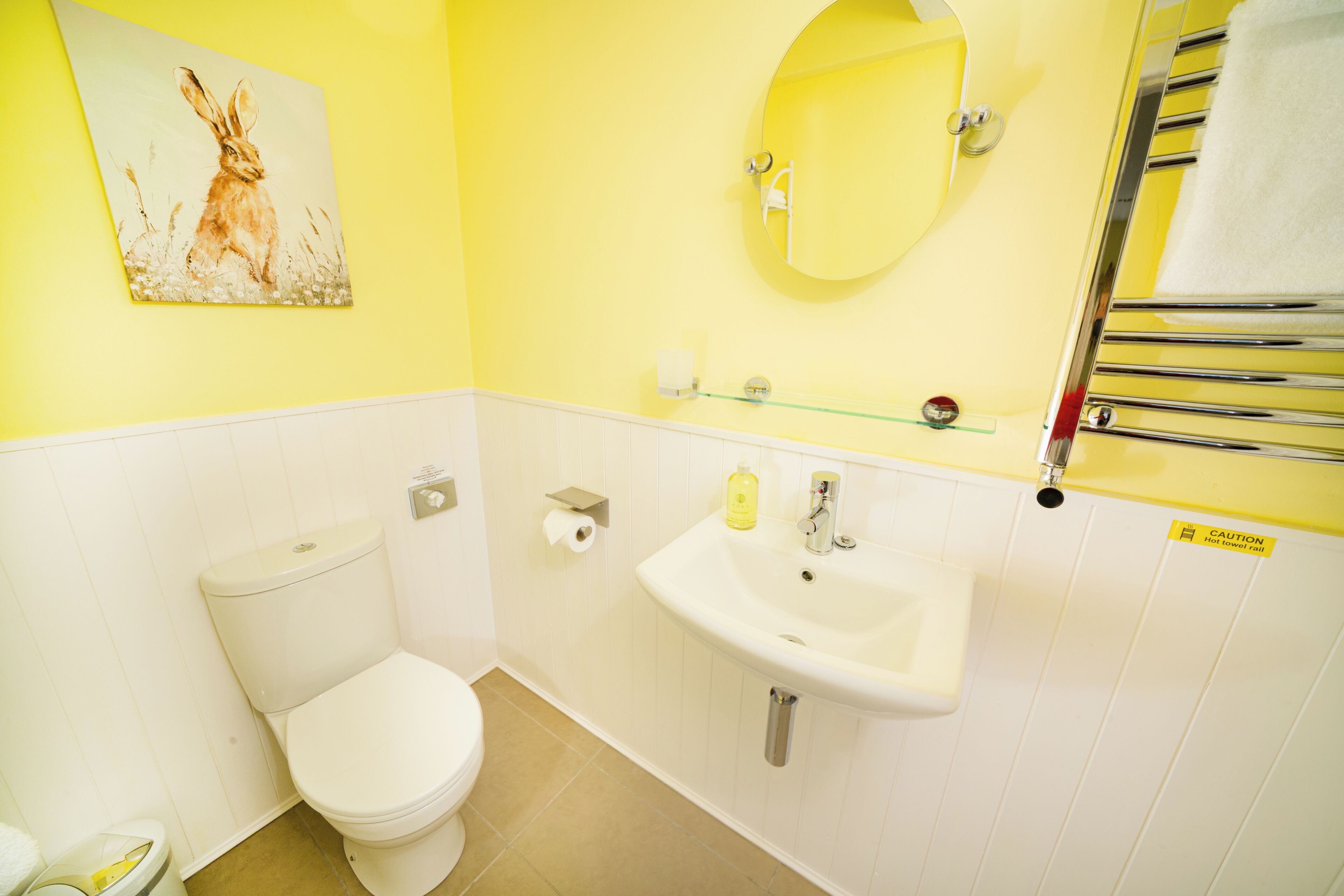 A bathroom with a toilet, sink, mirror, and towel rack.