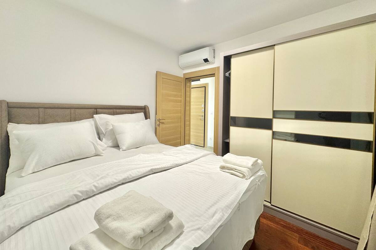 A neatly made bed with white linens, a bedside phone, and a folded towel.