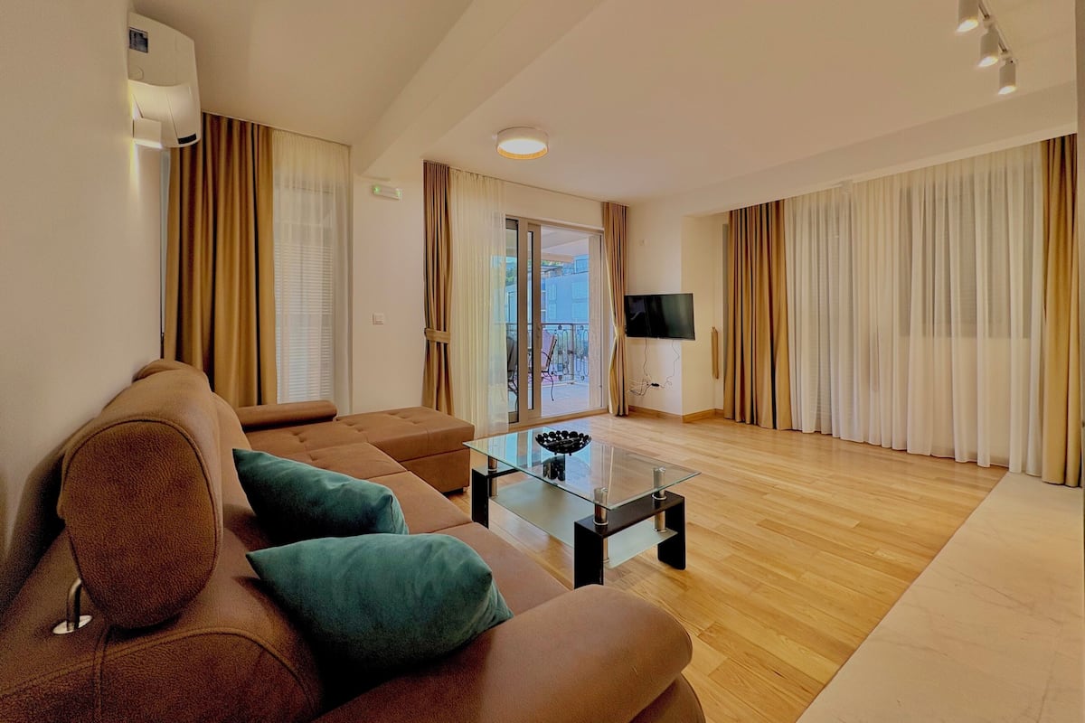 A modern living room with a brown sofa, a glass coffee table, and a flat-screen TV.