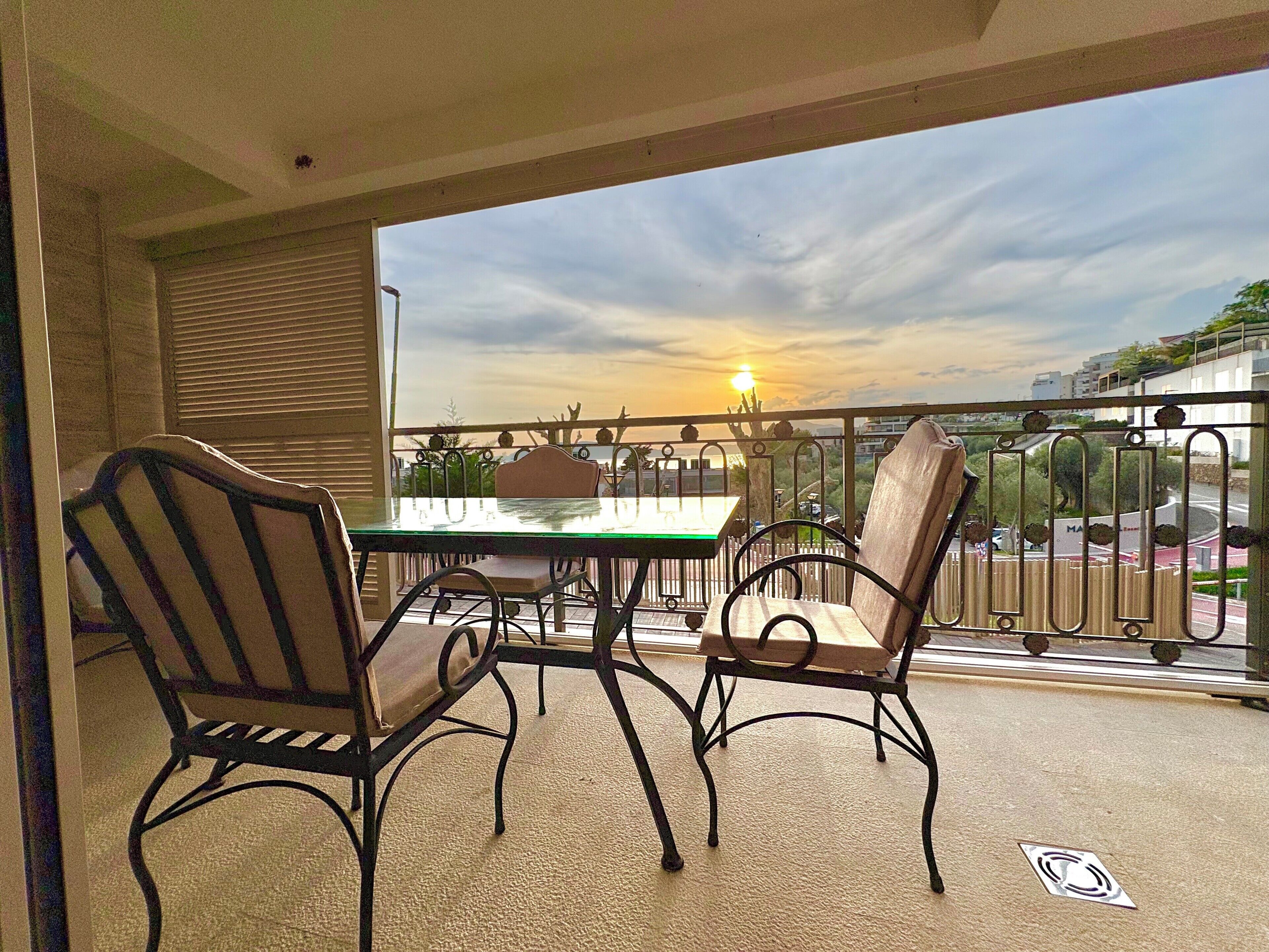 Een balkon met een tafel en stoelen, met uitzicht op een stadsbeeld in de zonsondergang.