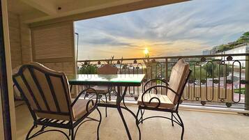 Een balkon met een tafel en stoelen, met uitzicht op een stadsbeeld in de zonsondergang.