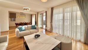 A modern living room with a sofa, a dining table, and a large window with curtains.