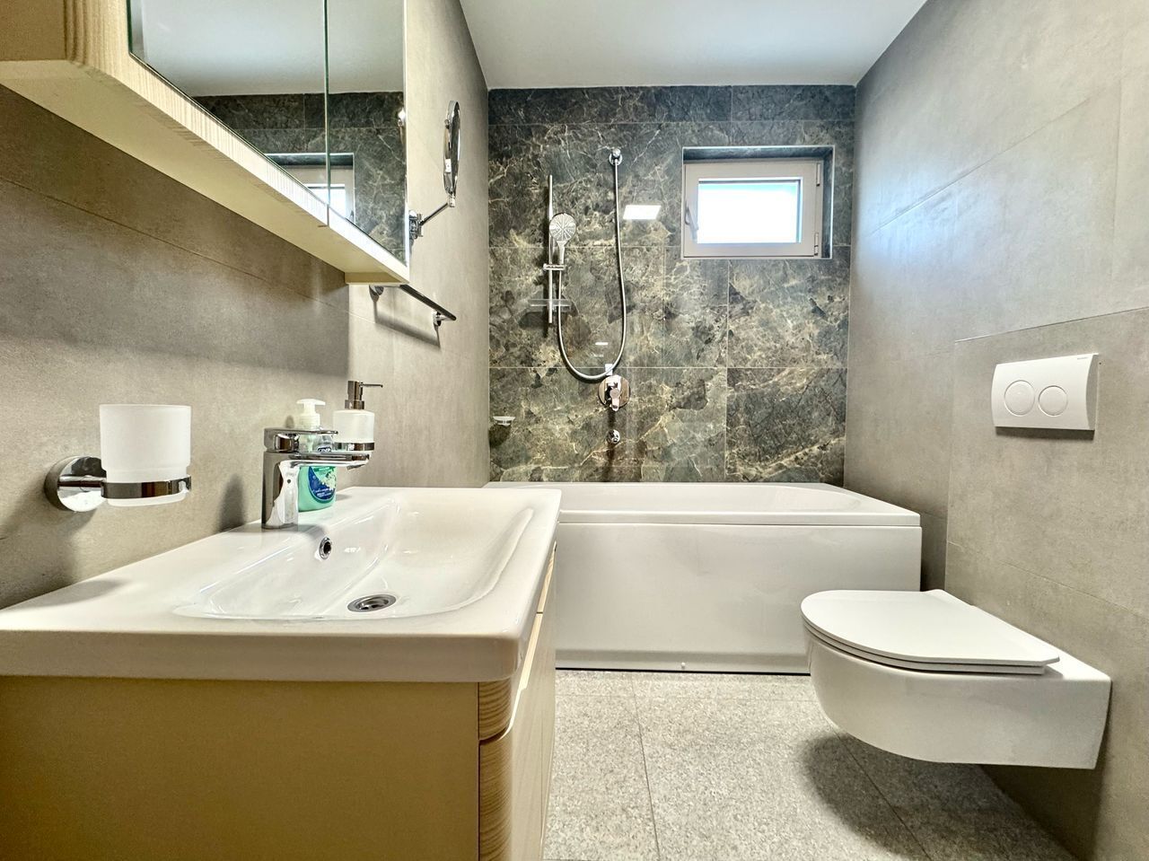 A modern bathroom with a marble backsplash, a freestanding bathtub, a toilet, and a sink with a mirror above it.