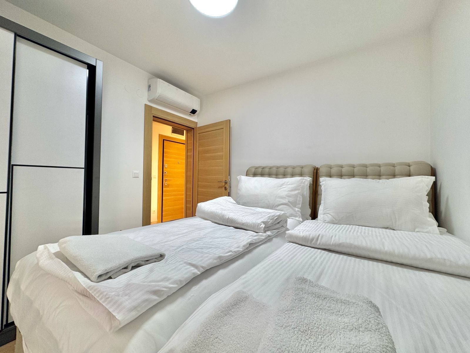 A bedroom with two beds, a wooden door, and an air conditioning unit.
