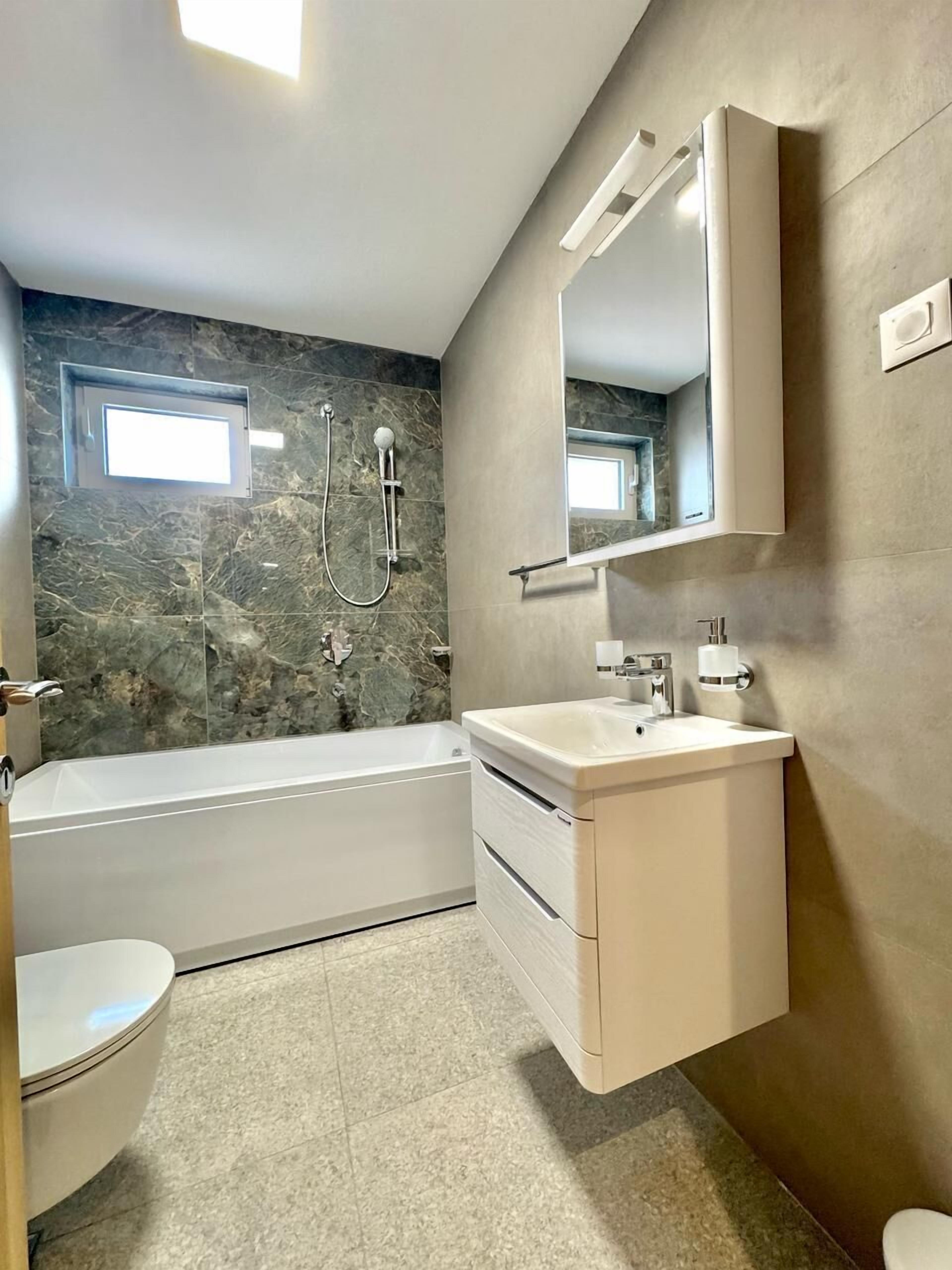 Une salle de bain moderne équipée d’une baignoire, de toilettes et d’un meuble-lavabo avec un miroir.