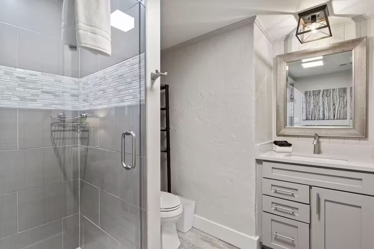 Een moderne badkamer met een douchecabine van glas, een wit toilet en een wastafel met lades en een spiegel.