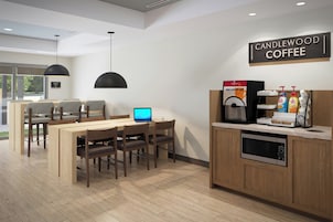 Interior moderno de una cafetería con zona de estar, una máquina de café y una computadora portátil sobre la mesa.
