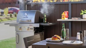 An outdoor grill with a burger on a plate, condiments, and a glass of water on a table. - Candlewood Suites Oakwood by IHG (Oakwood)