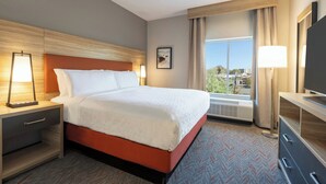 A hotel room with a bed, bedside tables, a desk, a chair, a TV, and a window with curtains. - Candlewood Suites Oakwood by IHG (Oakwood)