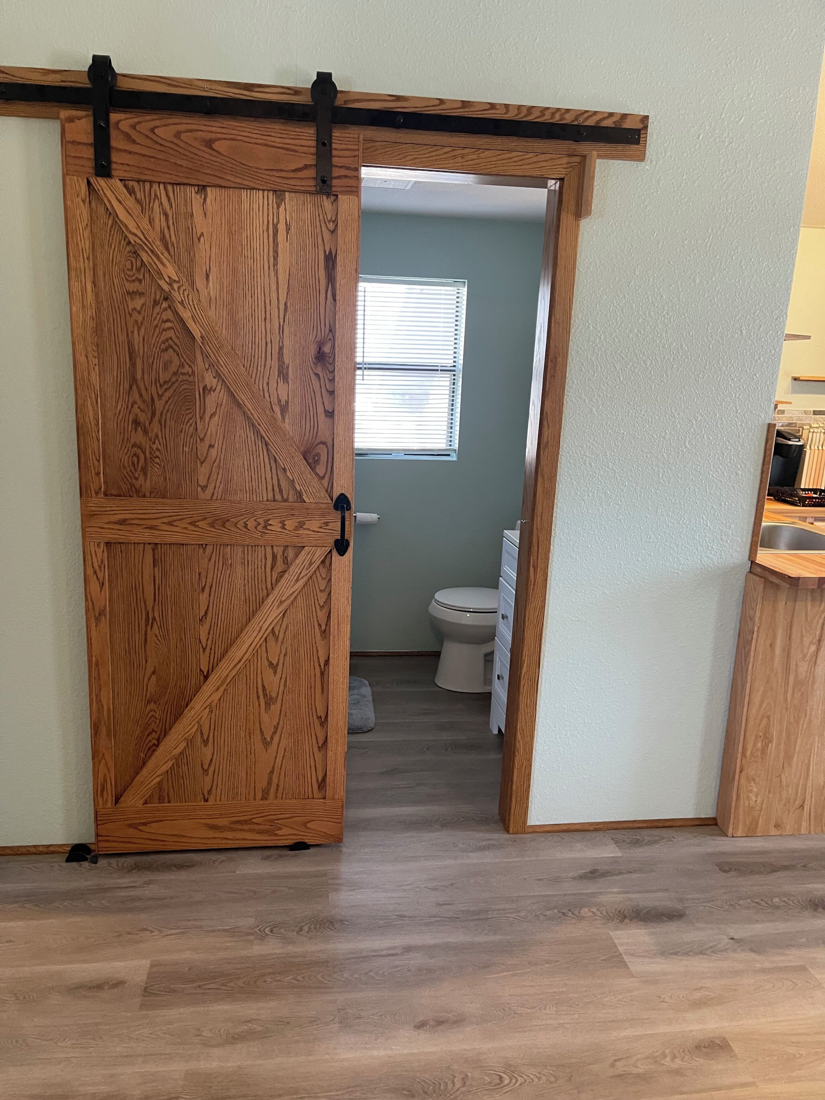 Une pièce dotée d’une porte coulissante en bois, de type porte de grange, qui donne accès à une salle de bain avec des toilettes et une fenêtre.