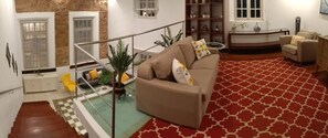 Cozy living area with a beige sofa, red patterned rug, and glass railing separating the space.