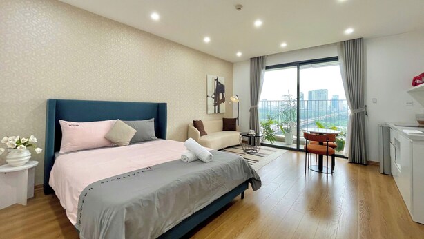 A modern bedroom with a large bed, a balcony with a view of the city, and a small dining area. - HN APT Vinhomes D'capitale Elegance (Hanoi)