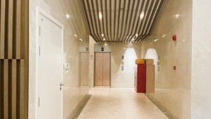 A modern elevator area with a marble floor, wooden paneling on the left, and a red pillar with luggage. - HN APT Vinhomes D'capitale Elegance (Hanoi)