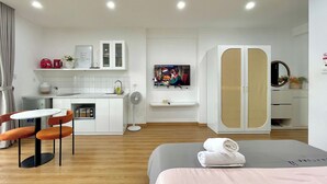 A modern hotel room with a bed, a small kitchenette, a dining area with a table and chairs, and a TV mounted on the wall. - HN APT Vinhomes D'capitale Elegance (Hanoi)