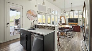 A modern kitchen with a central island, stainless steel appliances, and a dining area with a TV and seating. - Casa Sueño: Pool |SPA| Outdoor Movie ~ Golf Course (Austin)