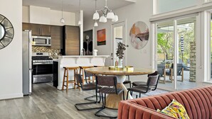 A modern kitchen with a dining area, a large window, and a living room with a sofa. - Casa Sueño: Pool |SPA| Outdoor Movie ~ Golf Course (Austin)