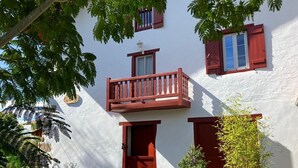 Ein weißes Gebäude mit roten Fensterläden, einem Balkon und Topfpflanzen.