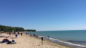 A beach with people walking and sunbathing, a clear sky, and calm water.