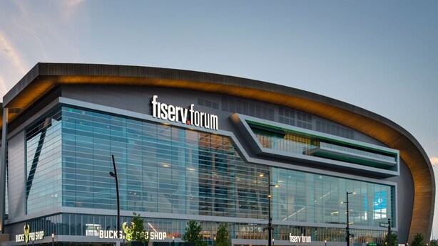 A modern building with a curved facade, large glass windows, and signage for 'fiserv forum' and 'BUCKS PRO SHOP'.