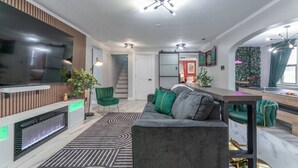 A modern living room with a flat-screen TV, a fireplace, a sofa, and a dining area with a table and chairs.