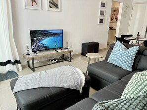 Una sala de estar moderna con un televisor de pantalla plana, sofá de cuero negro y un área de comedor al fondo.