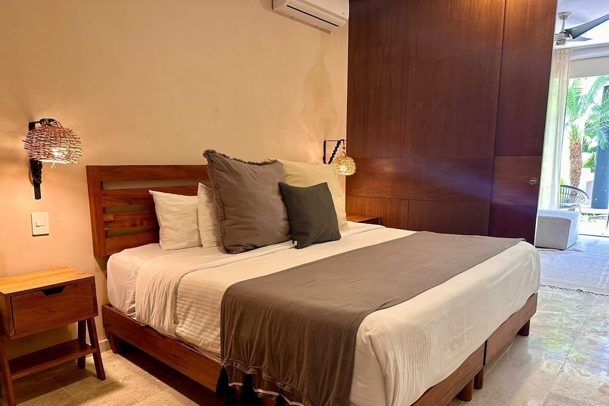 A neatly made bed with a wooden headboard, a bedside table, and a wall-mounted lamp.