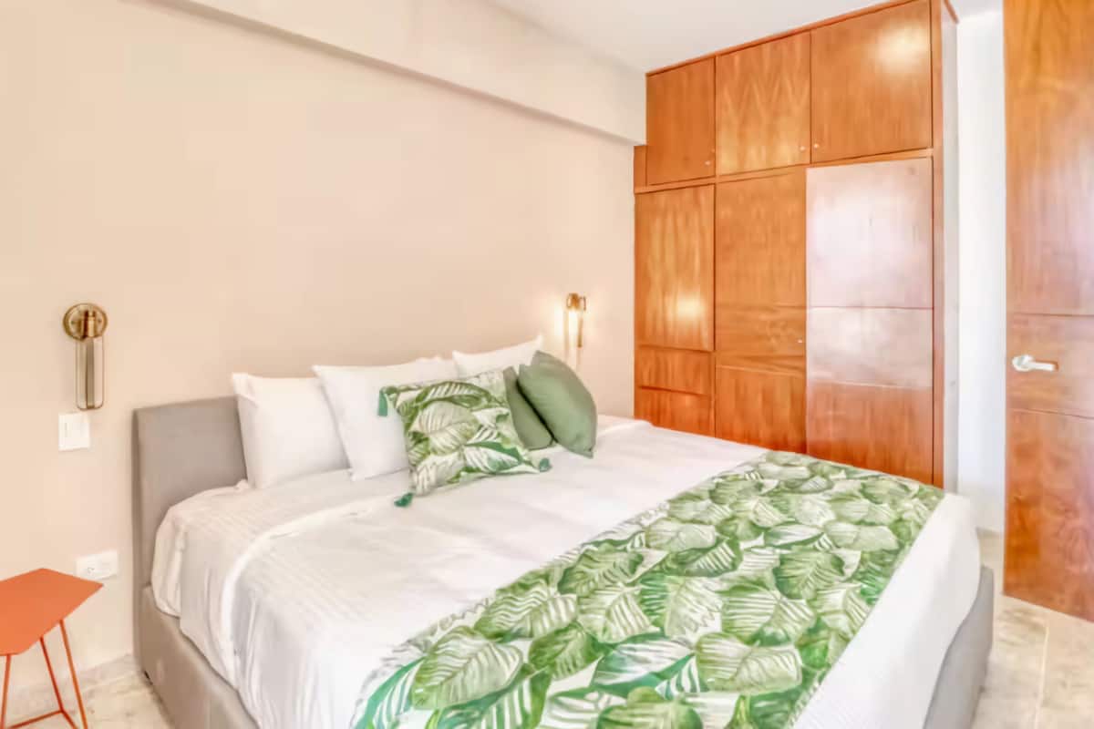 A bedroom with a bed, a nightstand, a wardrobe, and a wall-mounted light fixture.