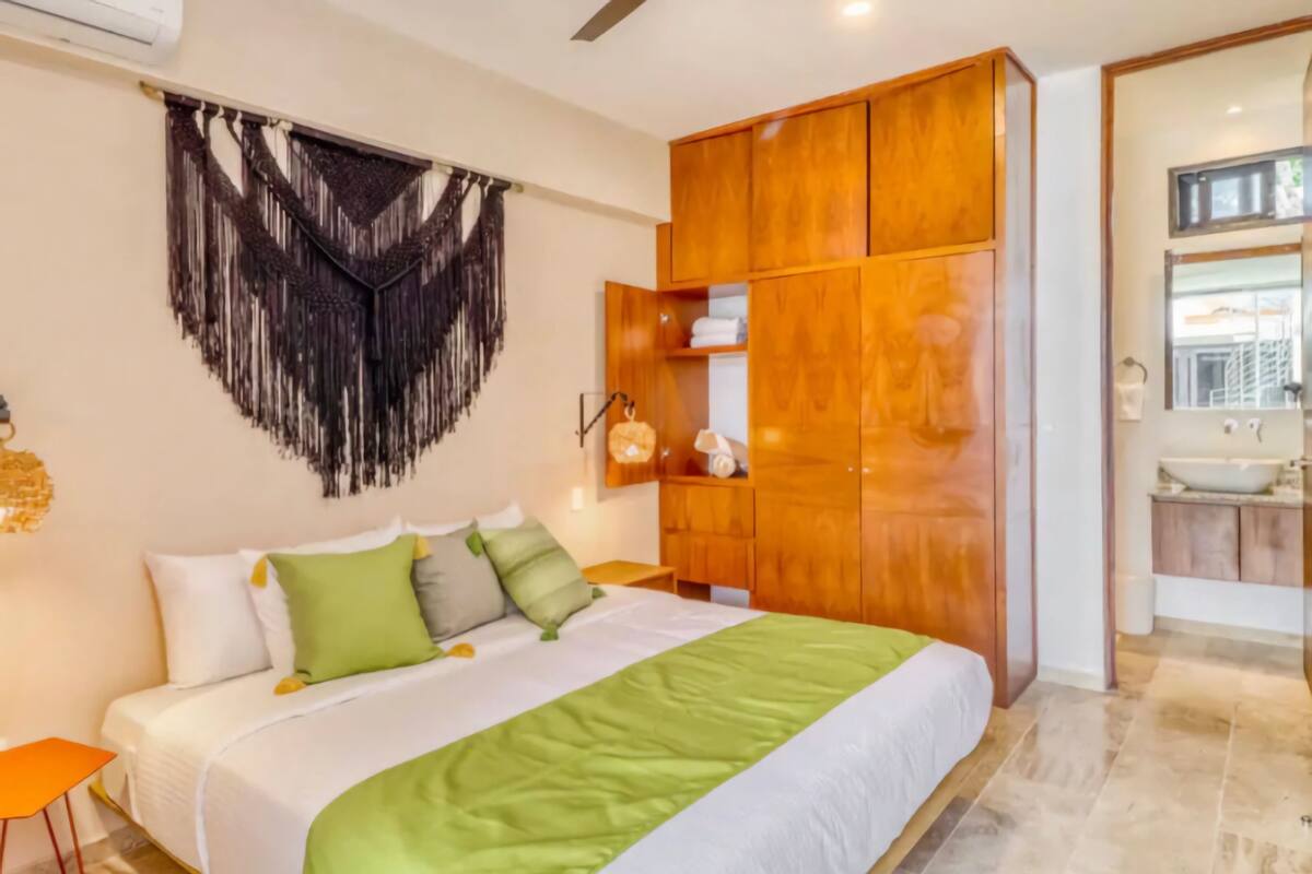 A bedroom with a large bed, wooden wardrobe, and a bathroom with a sink and mirror.