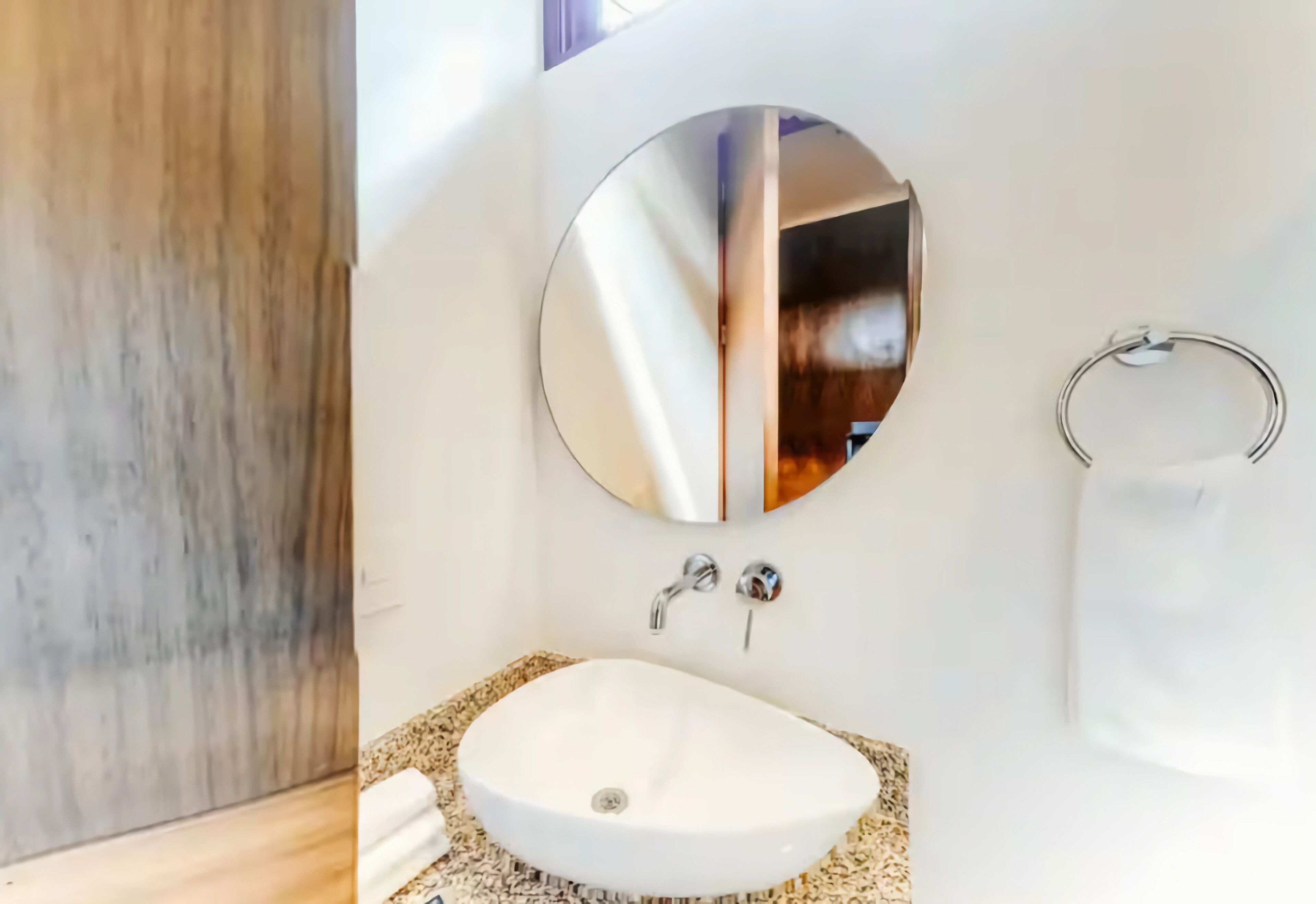 Une salle de bain avec un lavabo blanc, un miroir rond et un porte-serviette.