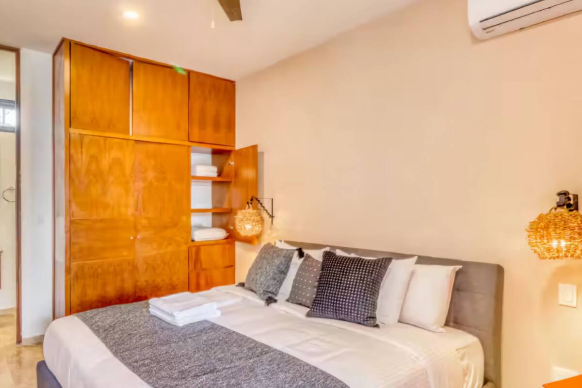 A bedroom with a bed, a wooden wardrobe, a bedside lamp, and a wall-mounted air conditioner.
