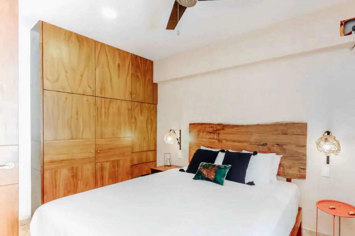 A bedroom with a large wooden wardrobe, a bed with white bedding, and a small red table.