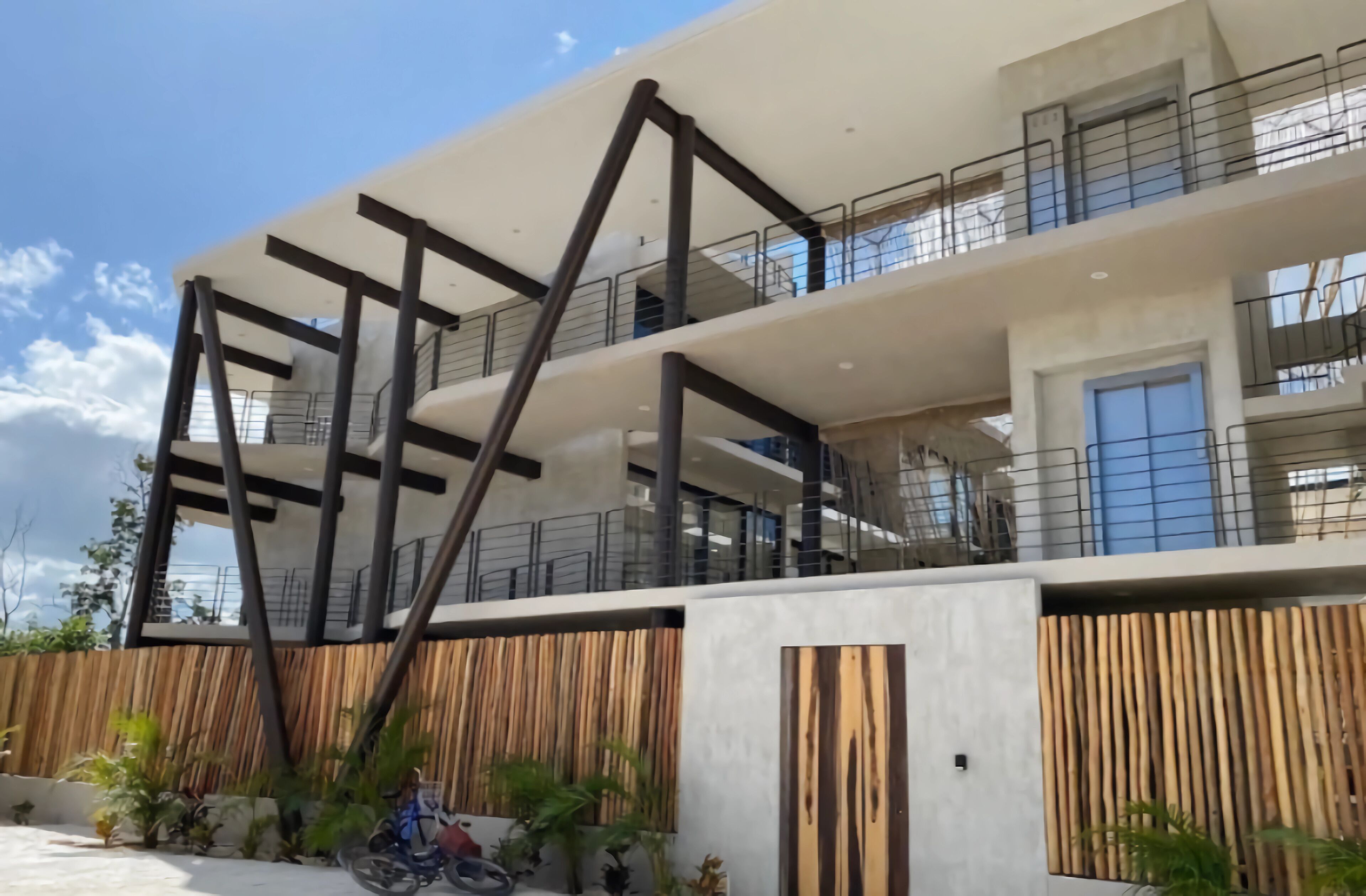A modern multi-story building with a minimalist design, featuring a prominent staircase and a wooden fence.