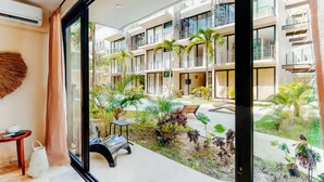 A modern hotel interior with a large glass window overlooking a courtyard with plants and a pool.