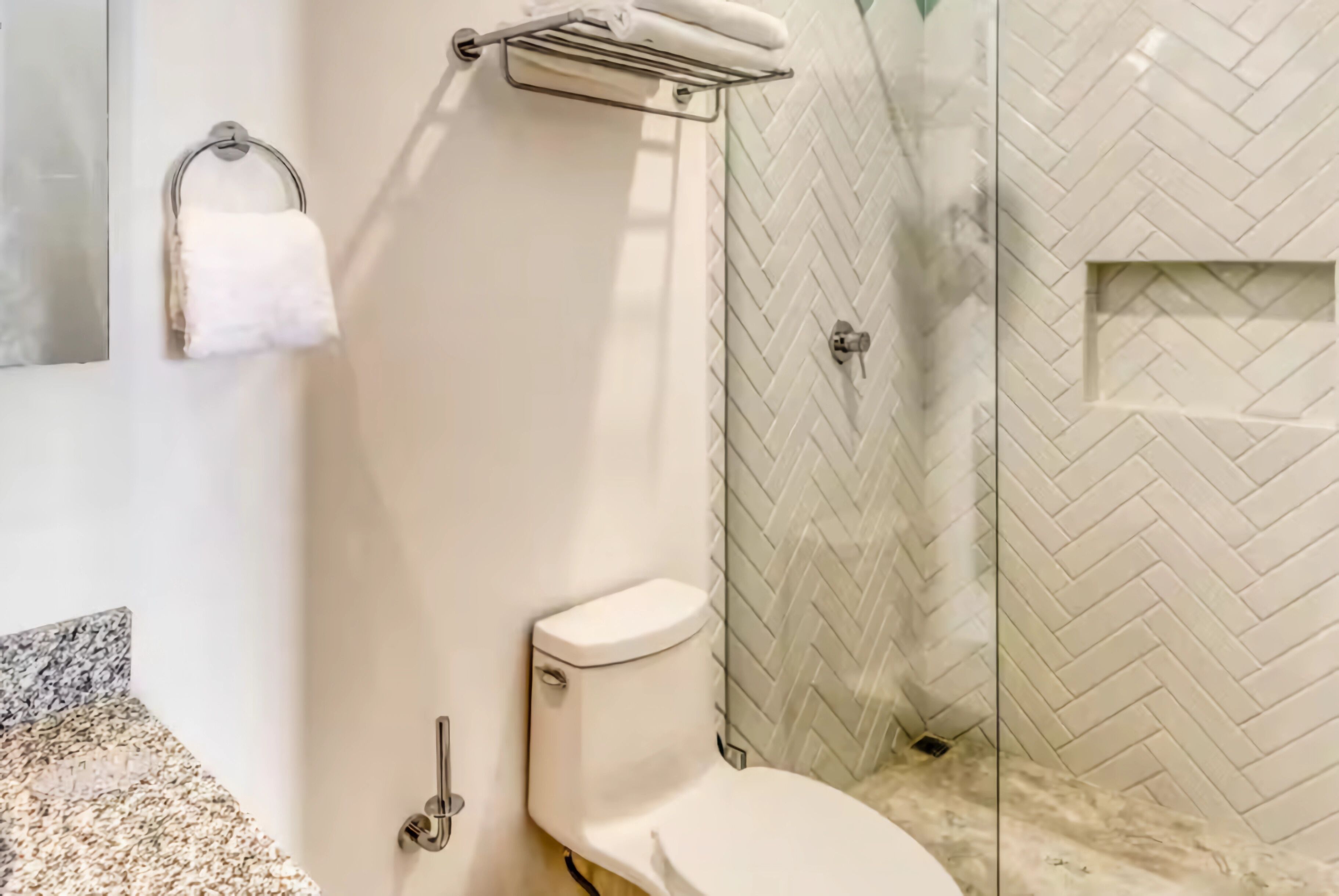 Une salle de bain comprenant des toilettes, un porte-serviettes et un espace douche avec un carrelage disposé en motif de chevrons.